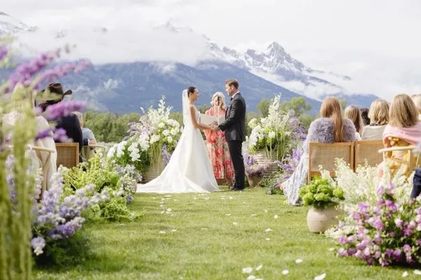 A wedding ceremony on a grassy lawn with abundant floral arrangements and the Tetons in the background.