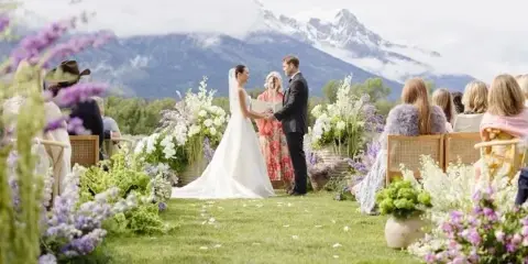 A wedding ceremony on a grassy lawn with abundant floral arrangements and the Tetons in the background.