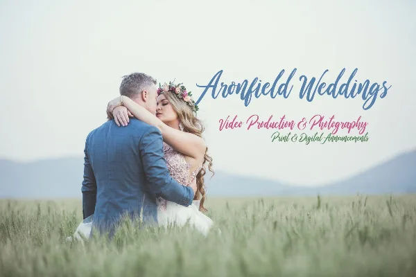 A bride and groom embracing in a grassy field with the Aronfield Weddings logo and text overlay.