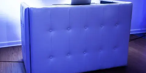 A white tufted DJ booth with a laptop on top, illuminated by blue and purple lighting.