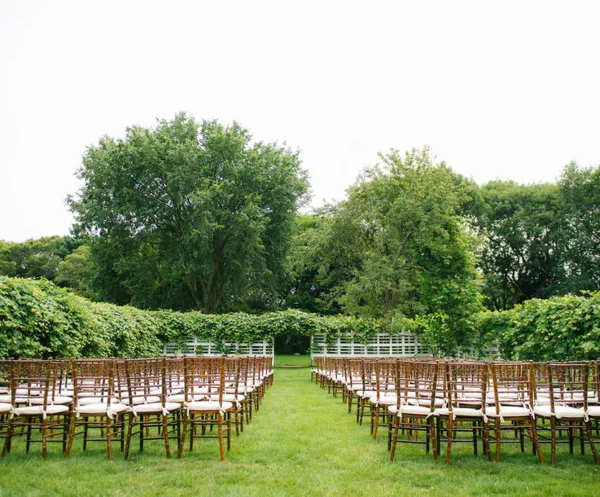 Outdoor wedding ceremony setup with rows of chairs and a white arch in a garden
