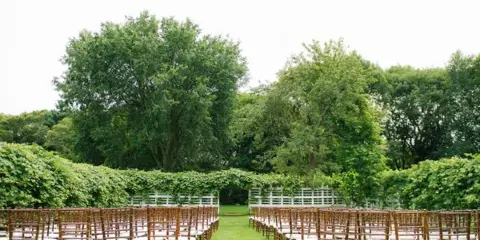 Outdoor wedding ceremony setup with rows of chairs and a white arch in a garden
