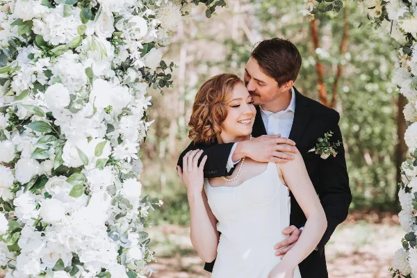 A bride and groom embracing under a floral archway during a wedding.