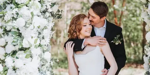 A bride and groom embracing under a floral archway during a wedding.