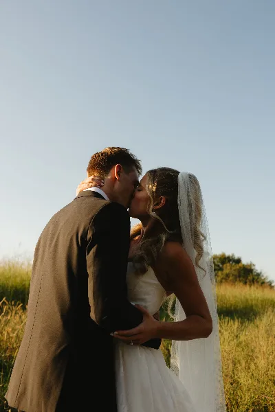 A bride and groom kissing in a field during golden hour.