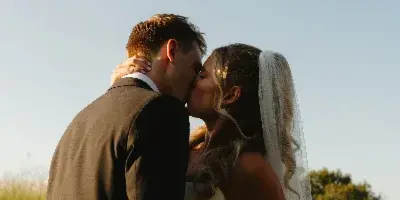 A bride and groom kissing in a field during golden hour.