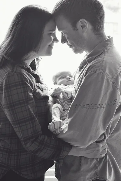 A black-and-white photograph of a couple holding a sleeping newborn baby.