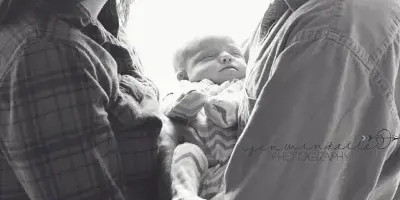 A black-and-white photograph of a couple holding a sleeping newborn baby.