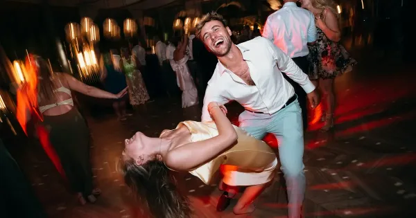 A couple dancing energetically on a wedding reception dance floor with other guests in the background.