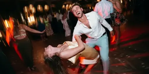 A couple dancing energetically on a wedding reception dance floor with other guests in the background.