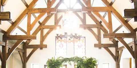 Interior view of a historic castle hall with exposed wooden beams and a stained-glass window during a wedding ceremony.