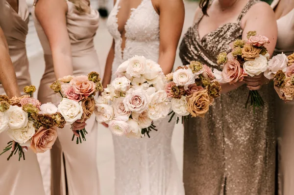 A row of bridesmaids and a bride holding matching wedding bouquets featuring white and blush roses.