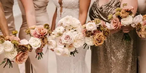 A row of bridesmaids and a bride holding matching wedding bouquets featuring white and blush roses.