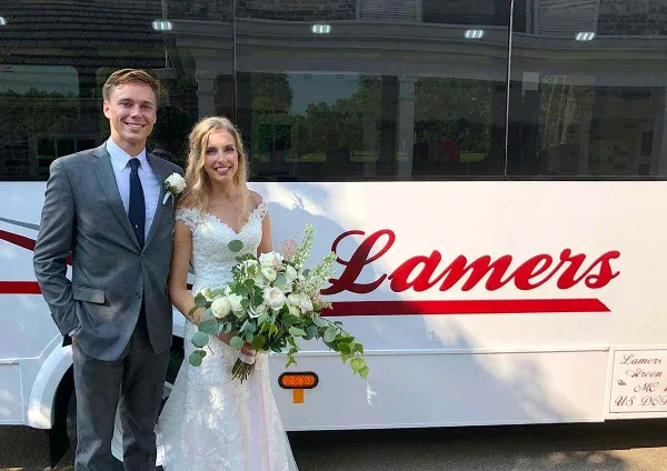 A bride and groom posing in front of a white Lamers bus