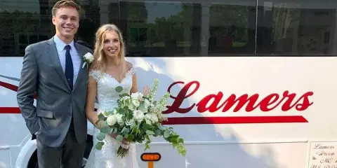 A bride and groom posing in front of a white Lamers bus