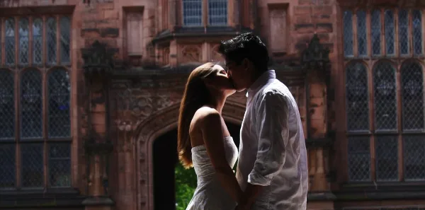 A bride and groom sharing a kiss in front of a large, ornate stone building.
