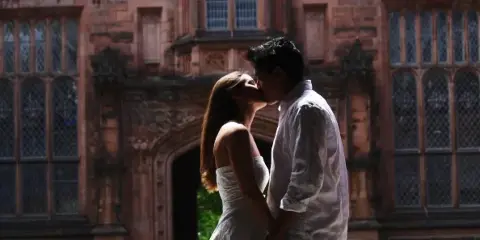 A bride and groom sharing a kiss in front of a large, ornate stone building.