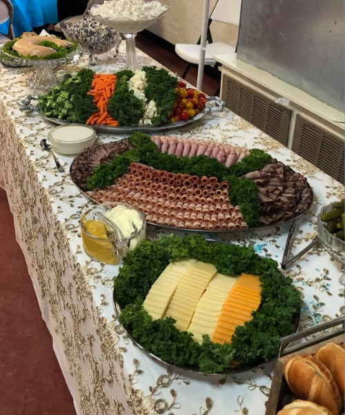 A catering table set with large platters of rolled meats, cheeses, and fresh vegetables.