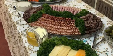 A catering table set with large platters of rolled meats, cheeses, and fresh vegetables.