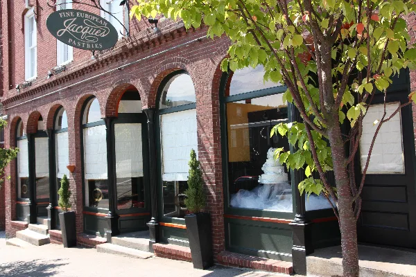 Exterior view of the Jacques Fine European Pastries storefront featuring a brick facade, arched windows, and a wedding cake display.