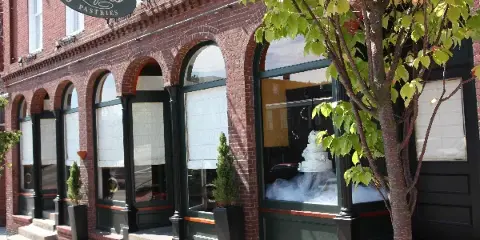 Exterior view of the Jacques Fine European Pastries storefront featuring a brick facade, arched windows, and a wedding cake display.