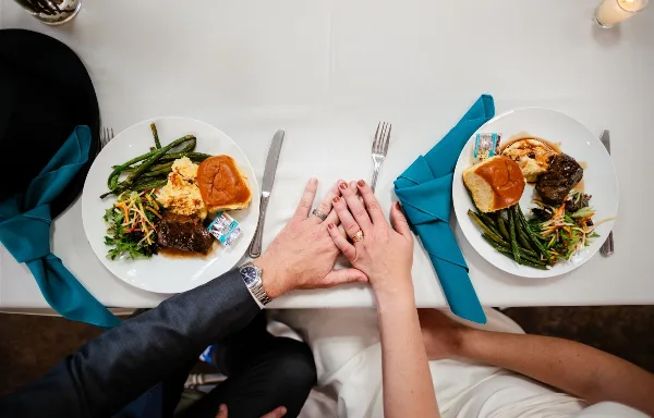 Overhead view of a couple holding hands at a table with plated meals of meat, potatoes, and vegetables.