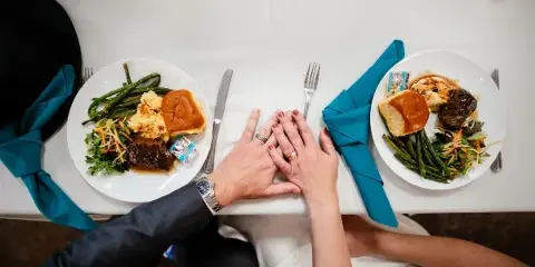 Overhead view of a couple holding hands at a table with plated meals of meat, potatoes, and vegetables.