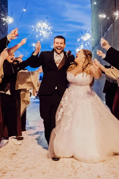 A bride and groom laughing and celebrating with sparklers at a wedding event.
