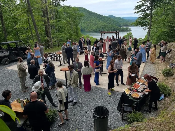 Guests gathered for a cocktail hour at an outdoor wedding venue overlooking a lake and mountains.