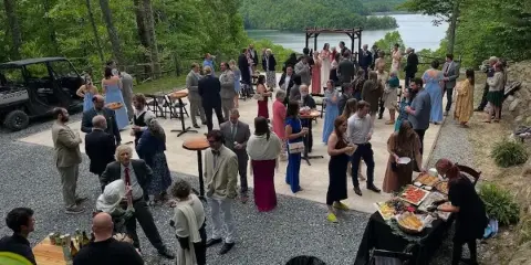 Guests gathered for a cocktail hour at an outdoor wedding venue overlooking a lake and mountains.