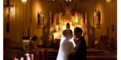 A bride and groom standing in the aisle of a church with stained glass windows and an altar in the background.