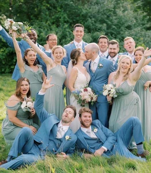 A wedding party consisting of a bride, groom, and wedding party members posing outdoors in a grassy field.