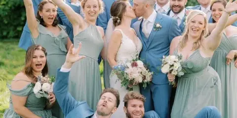 A wedding party consisting of a bride, groom, and wedding party members posing outdoors in a grassy field.