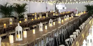 A long banquet table set with chairs, linens, and lanterns inside a white event tent.