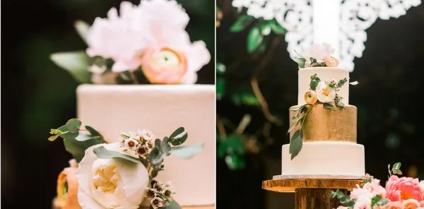 A multi-tiered white and gold wedding cake decorated with fresh flowers and greenery.