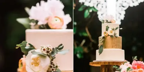A multi-tiered white and gold wedding cake decorated with fresh flowers and greenery.