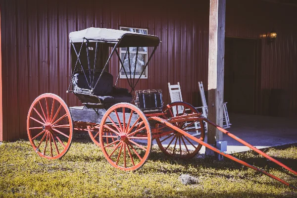 A red vintage carriage parked on a grassy area in front of a rustic red building.