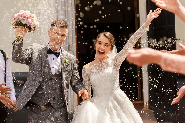 A bride and groom smiling and celebrating with a bouquet and confetti during a wedding.