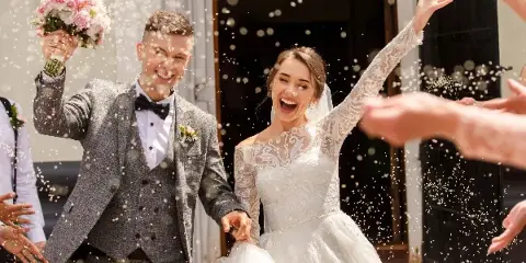 A bride and groom smiling and celebrating with a bouquet and confetti during a wedding.