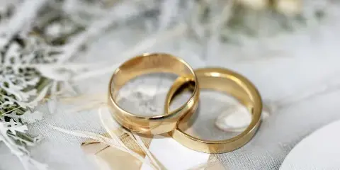 Two gold wedding rings resting on a white marriage license document with dried flowers in the background.