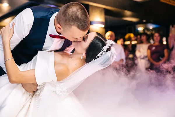 A bride and groom sharing a dip during their first dance at a wedding reception with guests and lighting in the background.