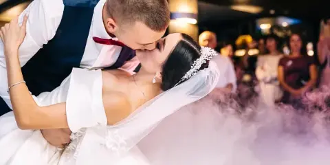 A bride and groom sharing a dip during their first dance at a wedding reception with guests and lighting in the background.