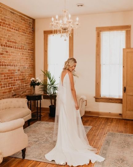 A bride in a white gown standing in a room with exposed brick walls, hardwood floors, and a chandelier.