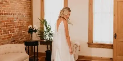 A bride in a white gown standing in a room with exposed brick walls, hardwood floors, and a chandelier.