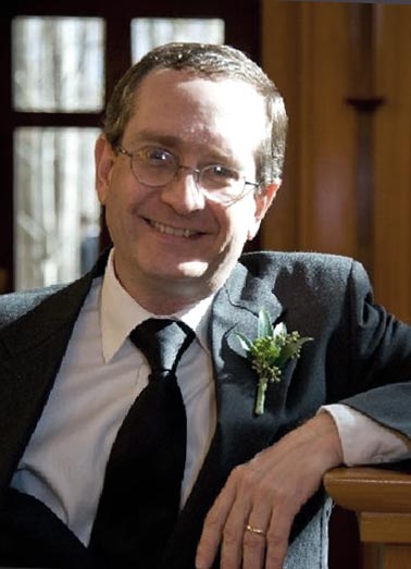 Portrait of a smiling man in a suit and tie wearing a boutonniere.