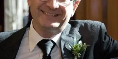 Portrait of a smiling man in a suit and tie wearing a boutonniere.