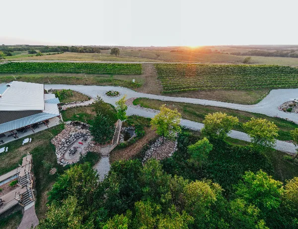 Aerial view of the Junto Wine winery property featuring vineyard rows, a large event center building, and landscaped grounds at sunset.