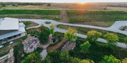 Aerial view of the Junto Wine winery property featuring vineyard rows, a large event center building, and landscaped grounds at sunset.