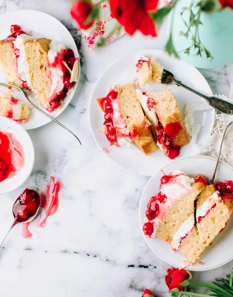 Slices of layered cake with cream and red fruit filling served on white plates with forks.