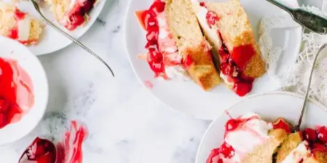 Slices of layered cake with cream and red fruit filling served on white plates with forks.
